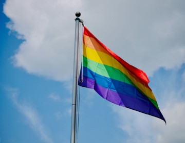 A rainbow-striped Pride flag flies against a blue sky background