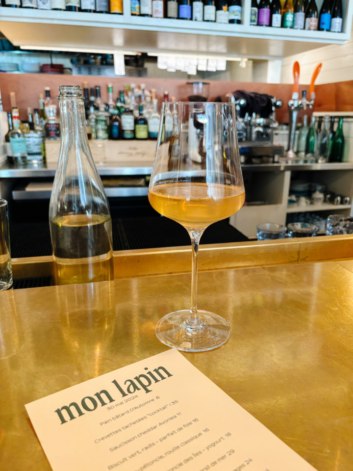 A glass of wine on the bar at Vin Mon Lapin with the menu from May 30 2024